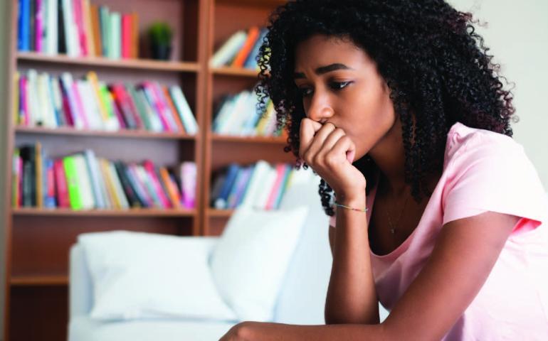 Anxious women sitting in a living room,  leaning into hand on her chin looking worried.